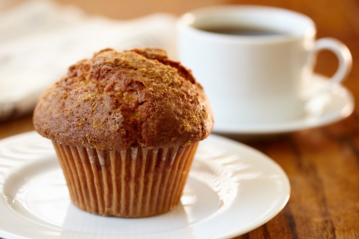 Cinnamon muffin shot with shallow focus with coffee and newspaper in background.