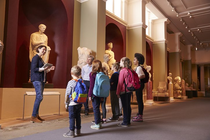 Pupils And Teacher On School Field Trip To Museum With Guide